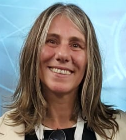 Fotografia de Manuela Francisco - uma mulher de cabelo castanho claro e olhos castanho a sorrir sobre um fundo azul claro. Vestida com uma camisola preta e blazer beje.