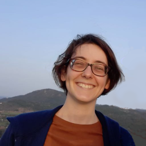 Fotografia de Patrícia Mendes - uma jovem adulta olha para nós com um sorriso aberto. Na paisagem, atrás, há uma montanha e o céu é límpido, azul-claro.