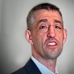 Fotografia de Norberto Sousa vestido com casaco preto e camisa branca. A pessoa tem cabelo curto ligeiramente grisalho, está barbeada e a sorrir. O fundo é de uma cor cinzenta clara, proporcionando um contraste que é comum em retratos profissionais ou corporativos.