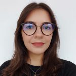 Fotografia de Daniele Miranda, uma mulher de cabelo castanho e olhos castanhos, com um sorriso suave e expressão acolhedora. Usa óculos de aros arrendondados e uma camisola preta, conferindo um ar profissional e moderno.