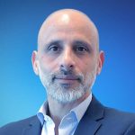 Fotografia de João Pina - homem careca e de barba grisalha bem cuidada com expressão serena e confiante. Veste um blazer azul-escuro sobre uma camisa clara, conferindo um aspeto profissional.