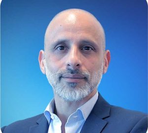 Fotografia de João Pina - homem careca e de barba grisalha bem cuidada com expressão serena e confiante. Veste um blazer azul-escuro sobre uma camisa clara, conferindo um aspeto profissional.