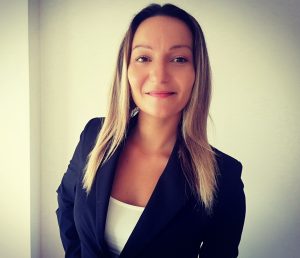 Fotografia de Soraia Arnaut Oliveira - uma mulher de cabelo loiro de expressão serena e confiante, a sorrir levemente para a câmara. Usa um blazer preto sobre um top branco, transmitindo uma aparência profissional e cuidado.