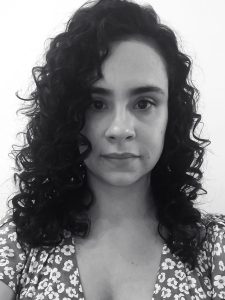 Fotografia de Camila Wohlmut, uma mulher com cabelo escuro encaracolado e olhos castanhos, com olhar sereno para a câmara. A fotografia é em preto e branco.