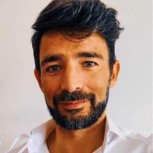 Fotografia de Bruno Godinho - homem de cabelo preto com barba bem cuidada com expressão serena e a sorrir ligeiramente. Veste uma camisa branca, conferindo um aspeto profissional.