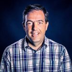Fotografia de Hélder Martins, um homem de cabelo negro e olhos castanho a sorrir para a câmara. Veste uma camisa e o fundo é de uma cor escura, conferindo um retrato profissional e moderno.