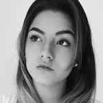 Fotografia de Lethícia Barros, uma mulher de cabelo escuro com madeixas a olhar levemente para o lado. A fotografia é a preto e branco.