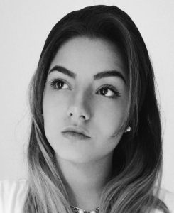 Fotografia de Lethícia Barros, uma mulher de cabelo escuro com madeixas a olhar levemente para o lado. A fotografia é a preto e branco.