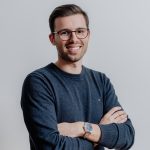 Fotografia de João Miguel Frazão Reis, um homem de olhos castanho e cabelo castanho claro arranjado. Usa óculos e encontra-se com os braços cruzados. O fundo é branco comum em fotos corporativas.