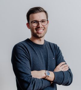 Fotografia de João Miguel Frazão Reis, um homem de olhos castanho e cabelo castanho claro arranjado. Usa óculos e encontra-se com os braços cruzados. O fundo é branco comum em fotos corporativas.