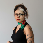 Fotografia de Margarida Miguel, uma mulher de olhos castanhos e cabelo castanho com madeixa branca na franja. Possui óculos e um lenço ao pescoço. O fundo é branco comum em retratos corporativos.