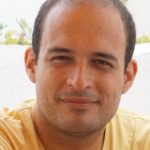 Fotografia de Nuno Próspero dos Santos, um homem de olhos castanhos e cabelo preto a sorrir levemente para a câmara.