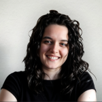 Foto de Teresa Fernandes, uma mulher de olhos castanhos e cabelo preto comprido ondulado, apresentando um largo sorriso para a câmera. O fundo é branco, comum em fotos corporativas.