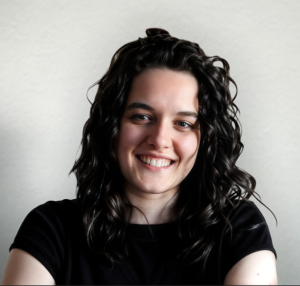 Foto de Teresa Fernandes, uma mulher de olhos castanhos e cabelo preto comprido ondulado, apresentando um largo sorriso para a câmera. O fundo é branco, comum em fotos corporativas.