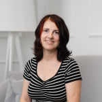 Fotografia de Teresa Mateus Alves, uma mulher de olhos castanho e cabelo preto com ligeiras madeixas vermelhas, a sorrir para a foto. O fundo é de cor branca, comum em retratos corporativos.