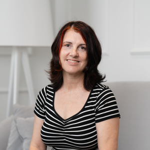 Fotografia de Teresa Mateus Alves, uma mulher de olhos castanho e cabelo preto com ligeiras madeixas vermelhas, a sorrir para a foto. O fundo é de cor branca, comum em retratos corporativos.