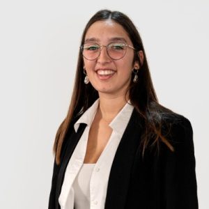 Fotografia de Ana Martins, uma mulher de cabelo castanho comprido a sorrir para a foto. Usa óculos arredondados e veste um blazer preto sobre uma camisa camisa, comum em fotos corporativas.