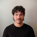 Fotografia de Daniel Alves, homem de olhos verdes e cabelo castanho com expressão serena para a câmara. Veste uma camisola preta e o fundo é cinza, conferindo um aspeto profissional comum em fotos corporativas.