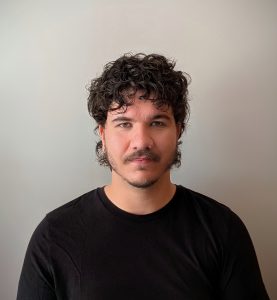 Fotografia de Daniel Alves, homem de olhos verdes e cabelo castanho com expressão serena para a câmara. Veste uma camisola preta e o fundo é cinza, conferindo um aspeto profissional comum em fotos corporativas.