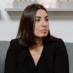 Fotografia de Carolina Alves, uma mulher de olhos e cabelo castanho escuro. Veste uma camisola preta e encontra-se de perfil para a câmara.